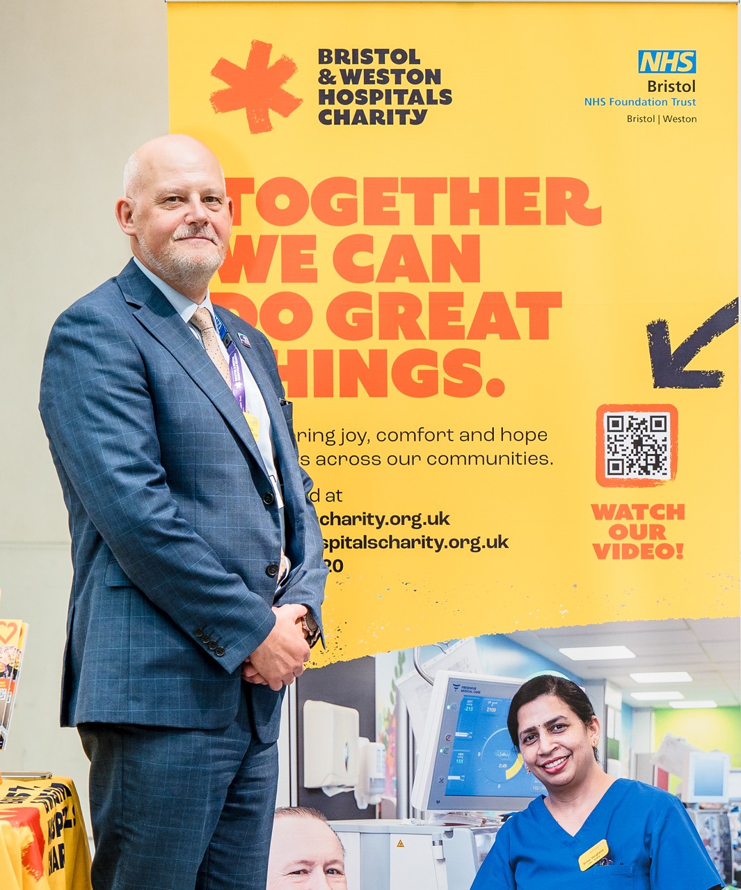 Glyn Howells standing beside a Bristol & Weston Hospitals Charity banner promoting a cycling fundraising challenge for Bristol NHS Foundation Trust