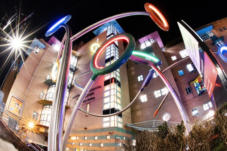 The front of Bristol Royal Hospital for Children at night, with the Hoops sculpture illuminated 