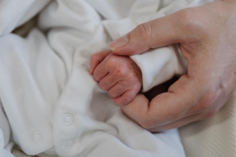 Newborn baby’s hand held gently by an adult hand