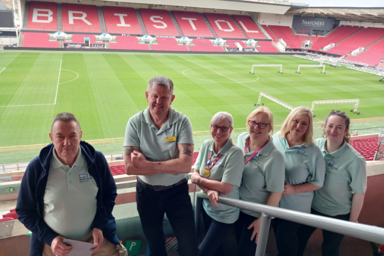 Bristol NHS Group colleagues smile for photo at Ashton Gate Stadium overlooking the pitch