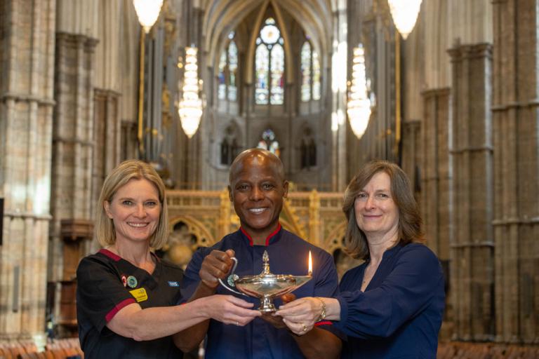 Three nurses smiling at camera holding a lamp at commemoration service