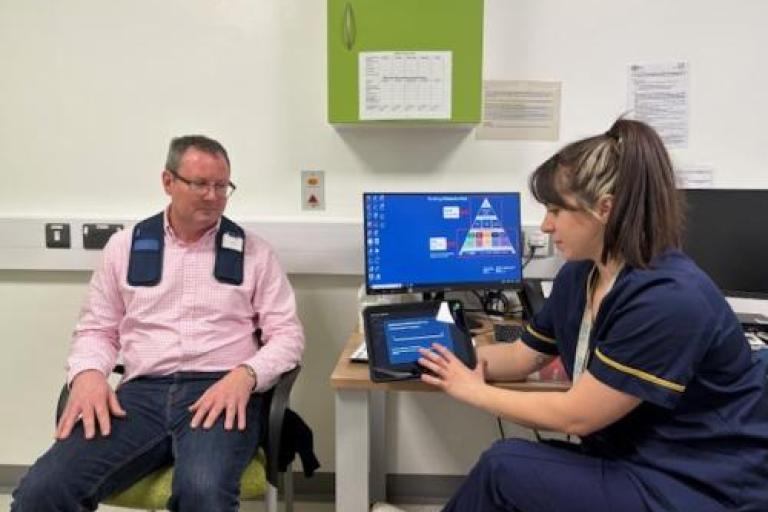 Patient John Morgan seated in a clinic while a clinician explains information displayed on a tablet