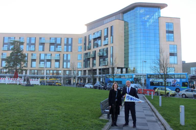 Maria Kane and Adam Tutton pose outside the Southmead Hospital Brunel Building. Adam is holding a Bristol Rovers flag.