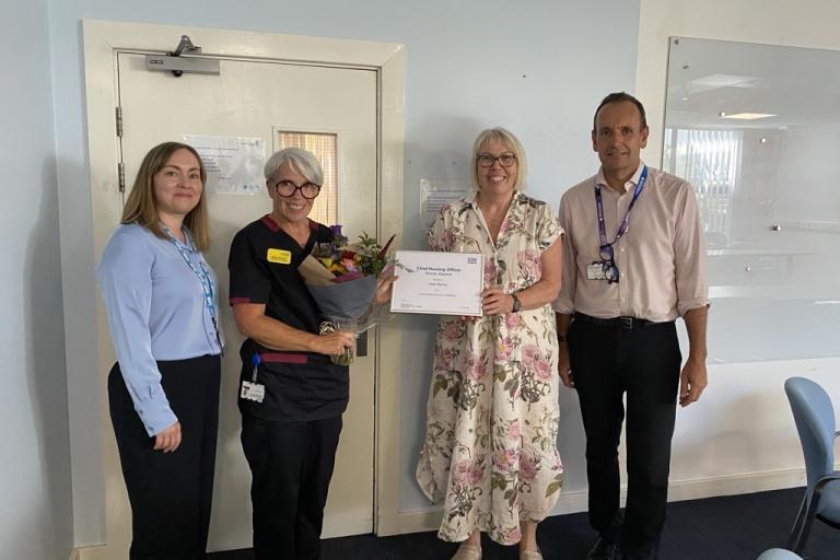 Helen Bishop stands with colleagues holding flowers and her CNO award 