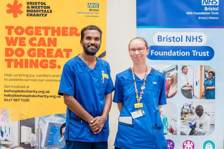 Two healthcare professionals are standing together. Behind them are two large pull up banners. 