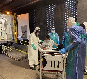 Simulation of a high-consequence infectious disease patient transfer with staff in protective suits assisting a seated patient into an ambulance