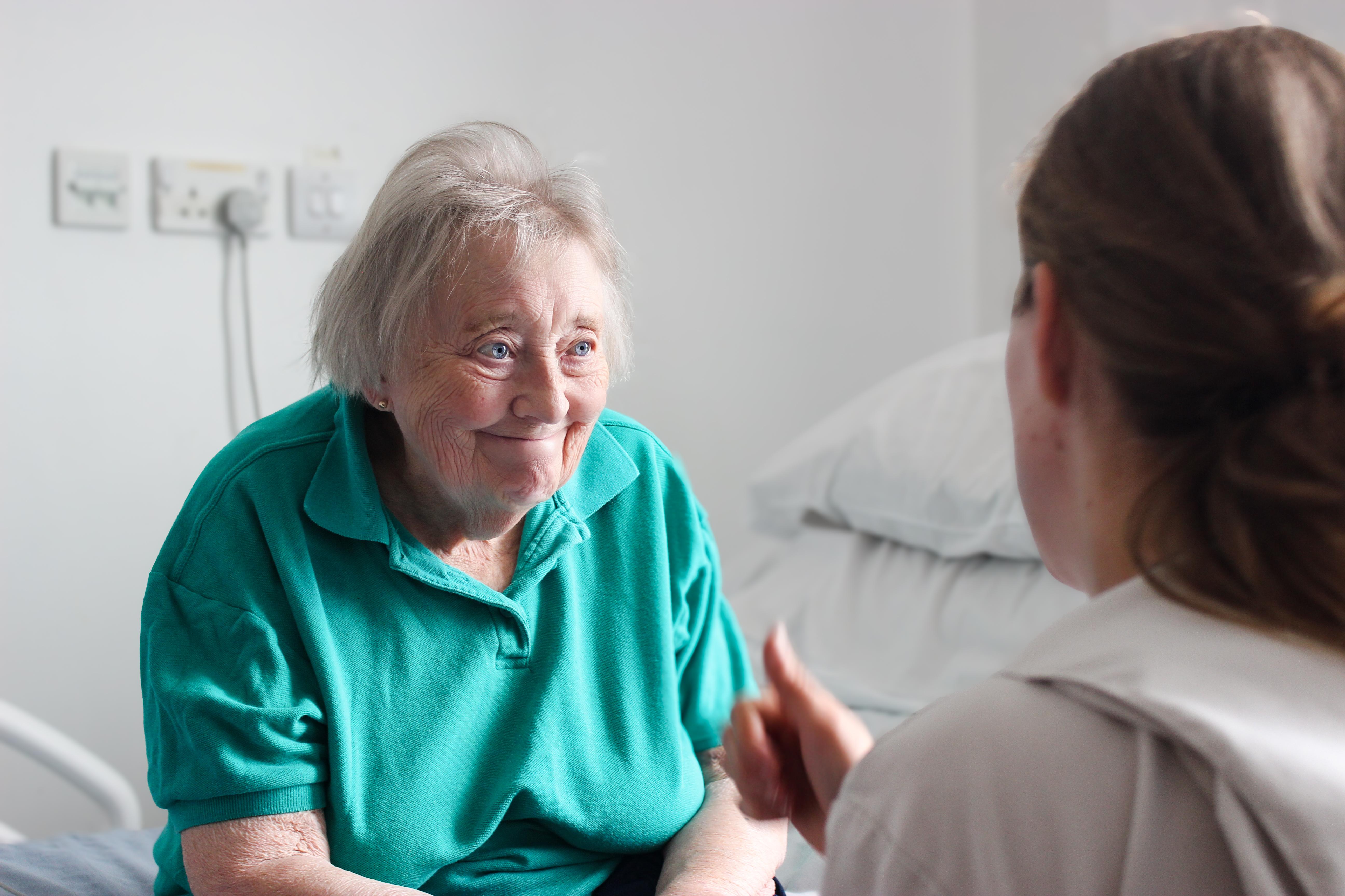 An older patient smiles at a healthcare professional in a clinical setting