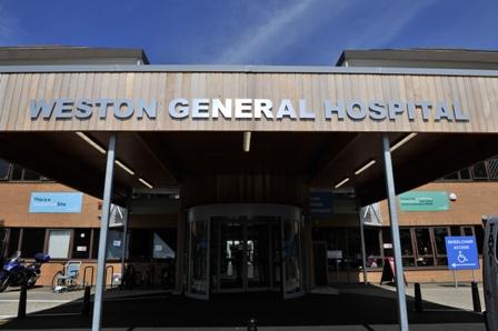 The main front entrance to Weston General Hospital, which includes a brown canopy with Weston General Hospital written in silver writing. Beneath the canopy are glass doors leading into the entrance of the hospital