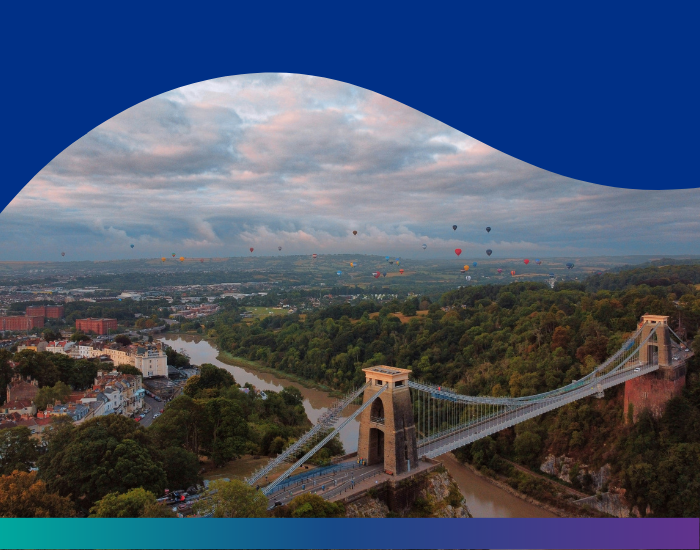 Photo looking out over the Avon gorge with Clifton suspension bridge in the foreground and hot air balloons in the background. 