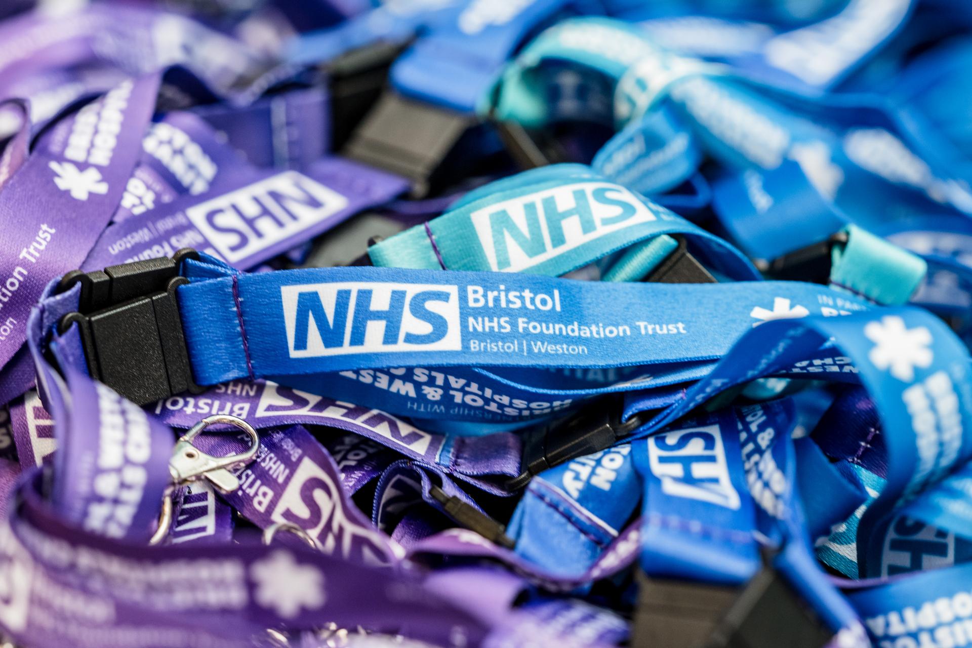 A pile of blus and purple lanyards, all featuring the Bristol NHS Foundation Trust logo