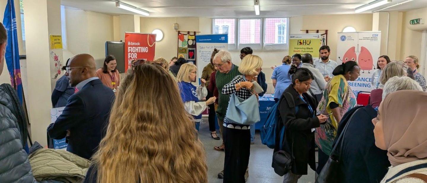 Lots of people are gathered in a room looking at information stands, and talking to each other.